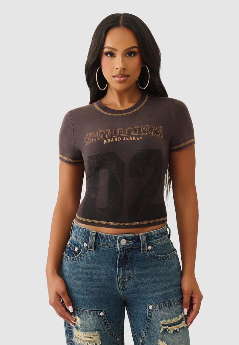 Czarny krótki T-shirt z złotym przeszyciem, z napisem "True Religion Brand Jeans" i dużą cyfrą "02". Noszony z przetartymi niebieskimi dżinsami.