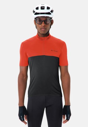 Mann trägt weißen Fahrradhelm, übergroße Sonnenbrille, rot-schwarzes Radsporttrikot, schwarze Handschuhe und schwarze Radsporthose, Blick nach vorne gerichtet.