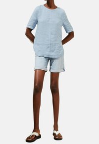 Ljusblå linnetopp i blandat material med korta ärmar, tillsammans med uppvikta denimshorts. Bärs med vita sandaler och ger en avslappnad sommarlook.