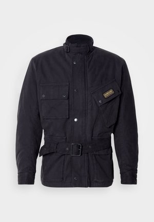 Schwarze gewachste Stoffjacke mit hohem Kragen, mehreren Taschen und Schnallen-Gürtel-Detail. Mit einem Logo-Patch auf der Brust.