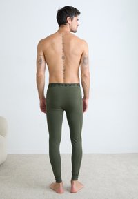 Green leggings made of smooth material, featuring a black waistband with "BJÖRN BORG" logo. The model is shown from the back.