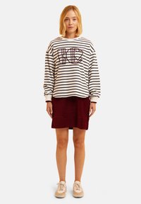 Sudadera a rayas blanca y navy con un gráfico de letras en un color llamativo, combinada con una falda de pana roja y zapatillas color crema. Atuendo informal.