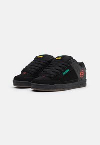 Zapatillas negras con construcción de ante y malla, que presentan la marca "GLOBE" en verde y amarillo, acentos rojos y una suela de goma texturizada.