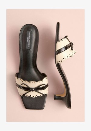 Čierne a krémové lodičky na vysokom podpätku so štvorcovou špičkou, vlnitým okrajom a lesklou koženkovou mašľou. Hladká textura a elegantný dizajn.