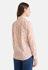 Camicia a bottoni floreale in pesca chiaro, con piccoli motivi di fiori rossi e verdi, colletto e maniche lunghe con polsini abbottonati.