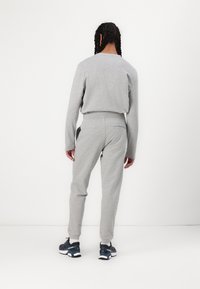 Light gray athletic outfit featuring a long-sleeve top and joggers, made of soft fabric with a relaxed fit. Signature accent on the back pocket.