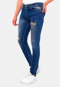 Dunne spijkerbroeken van denim met verwerkte accenten, een vijf-pocket ontwerp en een middelhoge taille, gecombineerd met witte sneakers.