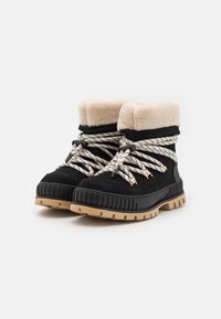 Bottes noires avec un col en fausse fourrure beige, dotées de lacets rayés blancs et noirs, de semelles en caoutchouc et de panneaux latéraux texturés.