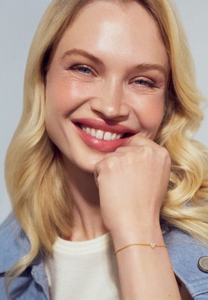 Guldkædearmbånd med et hjerteformet charms. Kæden er delikat, og charmsen har en klar ædelsten i midten.