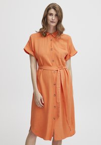Oranžové šaty na knoflíky vyrobené z lehké látky, s krátkými rukávy, opaskem v pase a náprsní kapsou na levé straně.