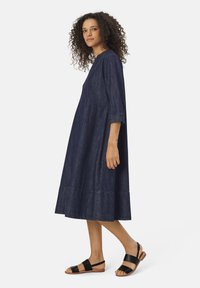 Laivan sininen farkkumeidät, jossa on kolme neljännes hihaa, löysä malli ja polven pituinen helma. Yhdistetty mustiin nahkasandaaleihin.