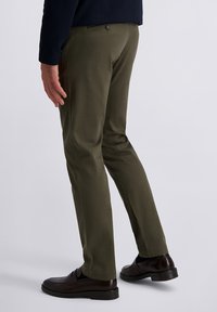 Olijfgroene, op maat gemaakte broek van een gladde stof, voorzien van een knoopsluiting en een slim fit. Geaccentueerd met bruine loafers.