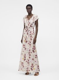 Mujer con vestido maxi sin mangas, con volantes, escote en V y estampado floral, cinturón atado a la cintura y sandalias abiertas, de pie sobre un fondo blanco liso.