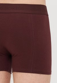 Close-up of person wearing fitted dark brown boxer briefs with branded elastic waistband.