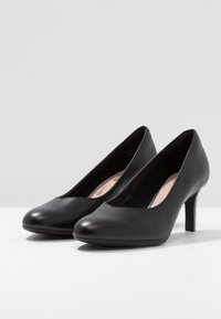Czarne skórzane buty na wysokim obcasie z okrągłym noskiem i gładką fakturą. Obcasy są smukłe i mają około 3 cale wysokości.