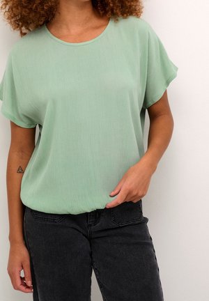 Haut vert menthe à manches courtes avec une coupe décontractée et une texture côtelée, porté avec un jean gris foncé. Il présente un col rond et un ourlet arrondi.