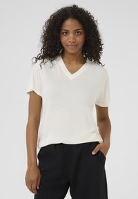 T-shirt blanc à col en V, en tissu léger, à manches courtes et à coupe décontractée, associé à un pantalon noir, mettant en avant une texture lisse.