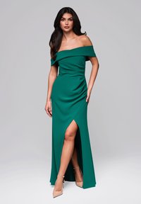 Grön aftonklänning med off-shoulder-design och en sidofåra, tillverkad av ett mjukt tyg. Klänningen har en figurnära överdel och en svävande kjol.