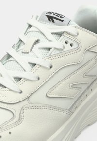 Białe skórzane sneakersy z panelami z siateczki, zaokrąglonym nosem, płaskimi sznurowadłami i logo na języku. Teksturowane akcenty wzbogacają design.