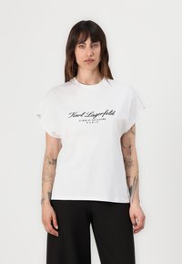 White cotton t-shirt with short sleeves and a crew neckline. Features black print: "Karl Lagerfeld 21 RUE ST. GUILLAUME PARIS" on the front.