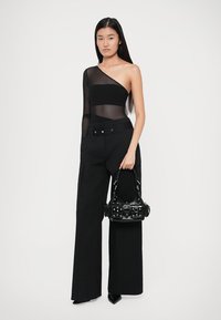 Top trasparente nero a spalla unica abbinato a pantaloni neri a gamba larga. Gli accessori includono una piccola borsa nera con dettagli metallici.