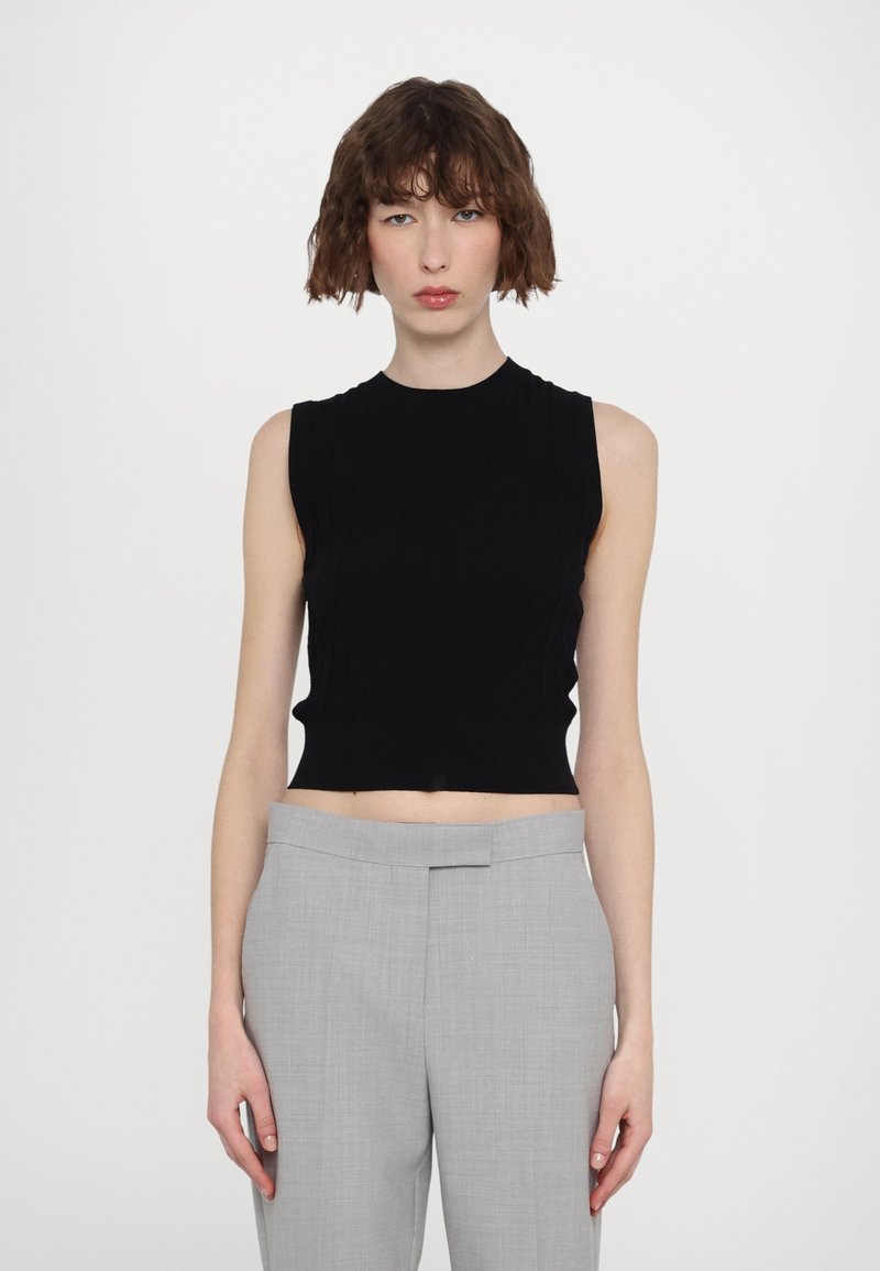 Haut noir sans manches en côtelé associé à un pantalon tailleur gris clair avec un devant plat et une texture de tissu lisse.