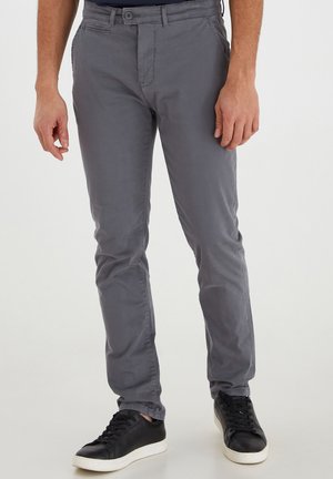 Szare bawełniane chinosy w slim fit, z zamek błyskawicznym, zapięciem na guzik i kieszeniami bocznymi. W połączeniu z czarnymi trampkami.