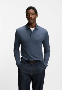 Koszulka polo z długim rękawem w kolorze granatowym, z kołnierzykiem i trzema guzikami. Na piersi subtelne logo, zestawiona z ciemnymi dżinsami.