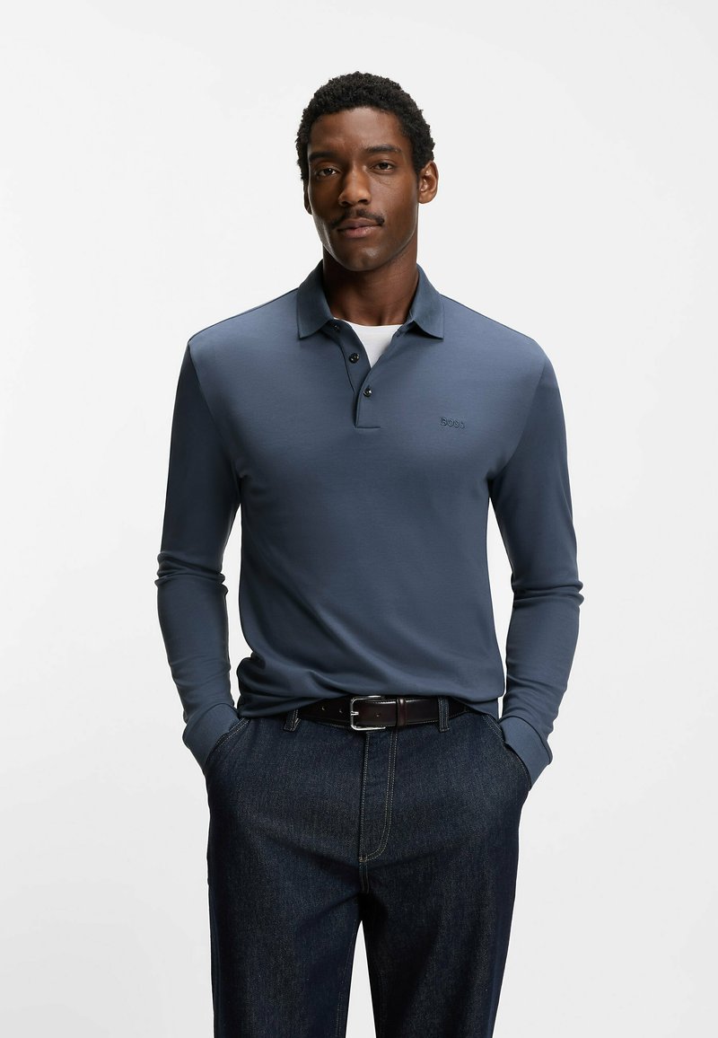 Koszulka polo z długim rękawem w kolorze granatowym, z kołnierzykiem i trzema guzikami. Na piersi subtelne logo, zestawiona z ciemnymi dżinsami.