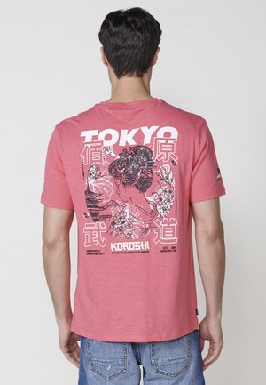 Camiseta de algodón roja con un gran diseño gráfico en la espalda, que representa a una mujer y texto, con cuello redondo y mangas cortas.