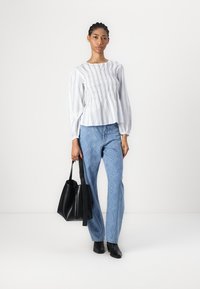 Hvit og blå stripete bluse med smocking-detaljer, kombinert med lyseblå mønstrede jeans. En svart tote bag og ankelstøvler fullfører antrekket.
