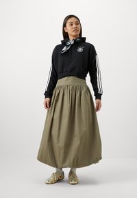 Sudadera negra corta con rayas blancas, falda alta color verde oliva y zapatos con estampado. Los accesorios incluyen una bufanda atada alrededor del cuello.