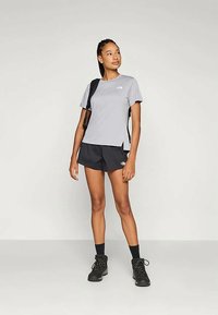 T-shirt cinza de manga curta, calções de desporto pretos e botins de caminhada pretos. Apresenta um logótipo na camisola, corte atlético e cabelo trançado.