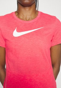 Camiseta rosa jaspeada con cuello redondo y manga corta. Presenta un prominente logo blanco de Nike swoosh en el pecho.