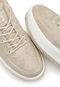 Beige Sneaker mit einem glatten Wildleder-Obermaterial, runder Zehenform und weißen Gummisohlen. Zu den Merkmalen gehören perforierte Details und Schnürverschluss.