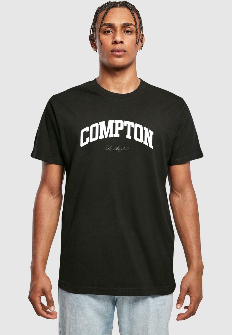 Sort bomulds T-shirt med fed hvid tekst "COMPTON" henover brystet og mindre "Los Angeles" nedenunder i kursiv skrifttype. Korte ærmer.