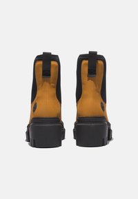Schwarze und gelbe Knöchelstiefel mit einem oberen Flächen aus glattem Leder, kontrastierendem strukturiertem Stoff, einer dicken schwarzen Sohle und einer Zuglasche an der Rückseite.