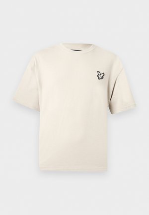 Kurzärmliges T-Shirt in Cremefarbe mit einem kleinen schwarz-weißen Vogelemblem auf der oberen linken Brustseite.