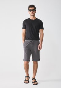 Svart kortermet t-skjorte parret med grå shorts med snor, rullede ermer og svarte sandaler. Elegant design med en uformell passform.