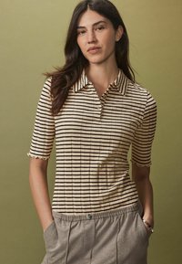 Polo en tricot avec une texture côtelée, présentant des rayures horizontales beige et marron, des manches courtes et un design de poignet à festons.