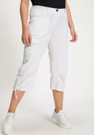 Pantalons cargo blancs coupés avec des poches latérales, des poignetres à cordon de serrage et une texture lisse. Associés à des baskets blanches et un haut noir.
