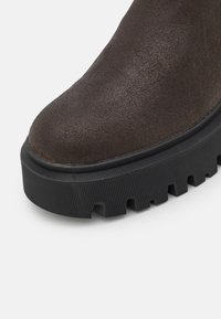 Gros bout de chaussure en daim brun foncé avec semelle en caoutchouc noire épaisse à rainures profondes et motif de bande de roulement prononcé.