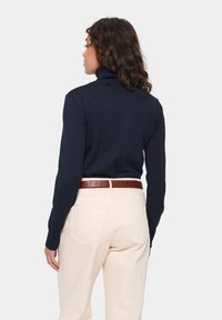 Navy turtleneck sweater with ribbed texture, paired with high-waisted cream pants. A brown textured belt completes the outfit.