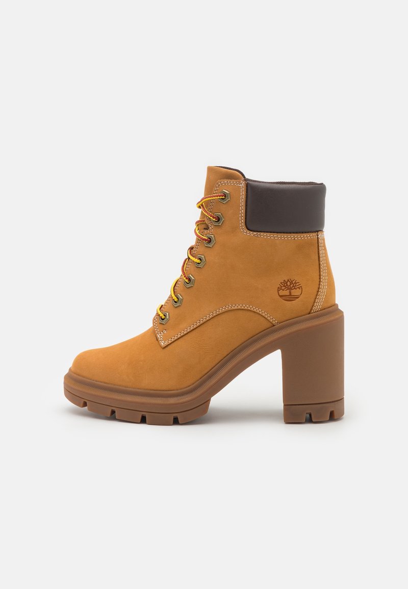 Bottine beige à lacets avec col matelassé marron foncé, talon haut épais, semelle robuste et logo arbre Timberland sur le côté.