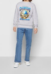 Felpa grigia con un grande graphic colorato con il testo "CHAMPIONS", abbinata a jeans blu e sneaker bianche con accenti gialli e blu.