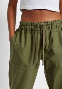 Vihreät pellavahousut, joissa on elastinen vyötärökaitale kiristysnauhalla, kaksi sivutaskua ja rento istuvuus.