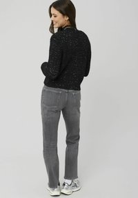 Pull noir texturé avec fil métallique, associé à un jean gris et des baskets blanches. Le pull a un ourlet côtelé et une coupe décontractée.