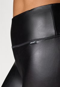 Schwarze hochgeschnittene Leggings aus glattem, dehnbarem Material mit DKNY-Logoschildchen in der Nähe des Bunds und flachen Nähten für zusätzlichen Komfort.