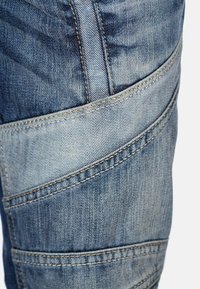 Jeans in denim blu con un motivo texture, dotati di cuciture a contrasto e tasche angolate, che mostrano un design classico e un tessuto resistente.