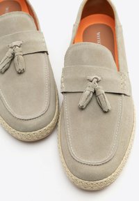 Grijze suède loafers met kwastjes, voorzien van een espadrille jute zool en een oranje binnenzool. Glad oppervlak en klassieke ontwerpdetails.